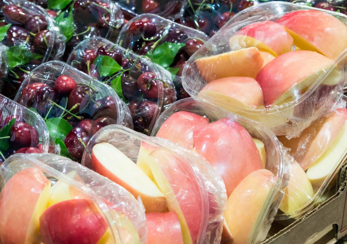 Solutions d'emballage alimentaire efficaces et durables en 2025 4 Barquettes de cerises noires et de pommes rouges tranchées exposées au marché, emballées sous film plastique transparent.