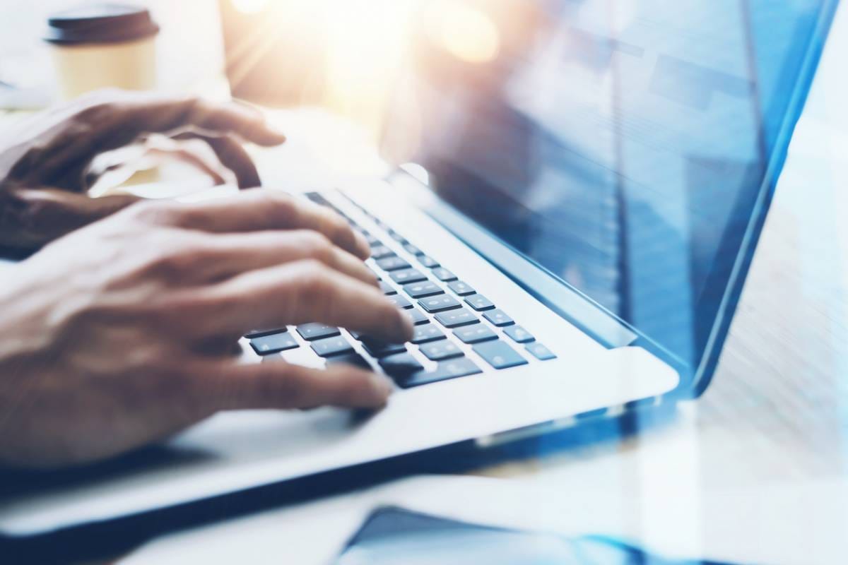 Mains tapant sur un clavier d'ordinateur portable bleu, avec une tasse de café en arrière-plan, illustrant un environnement de travail numérique avec système d'information fiable.