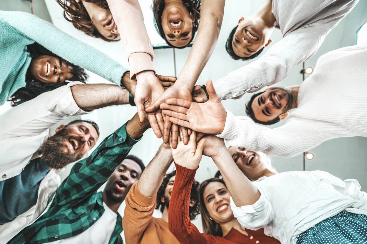 Les lieux immersifs qui rendent votre événement d'entreprise mémorable 4 Groupe diversifié de personnes souriantes formant un cercle et unissant leurs mains au centre, vue de dessous symbolisant l'unité et la collaboration en événement entreprise.