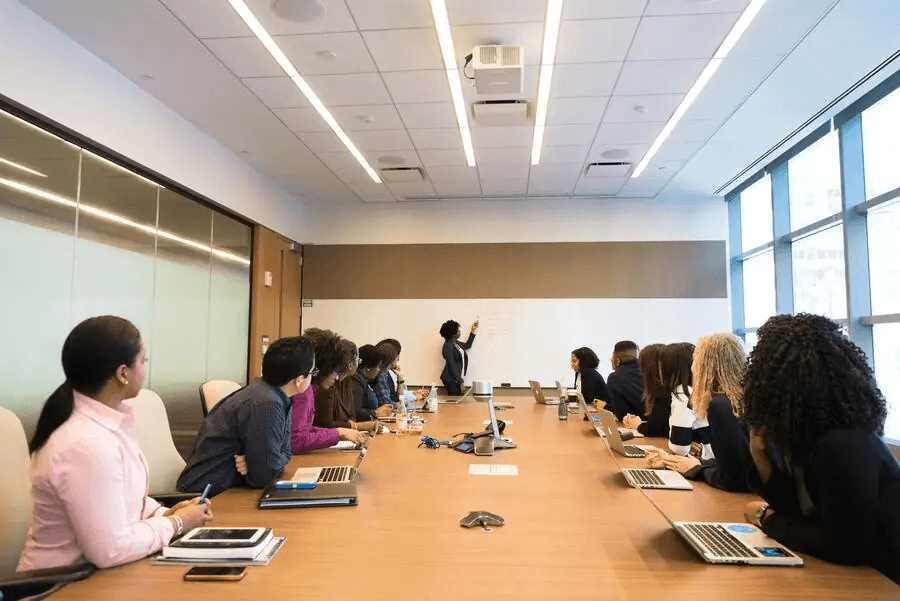 Pourquoi les noms de marque doivent-ils désormais anticiper les conflits de domaine plus tôt ? 4 Salle de conférence moderne avec groupe de professionnels assis autour d'une table en bois, équipés d'ordinateurs portables et tablettes, lors d'une réunion d'affaires.