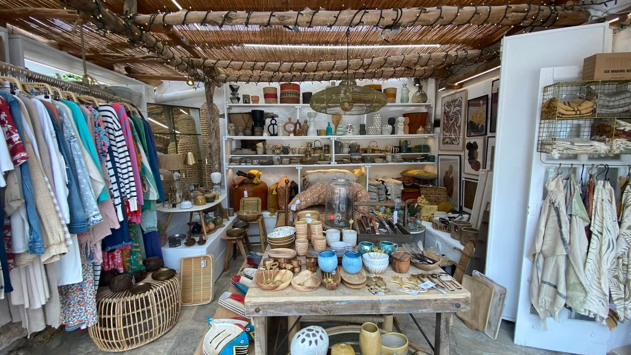 Décoration de boutique : pourquoi les commerçants misent sur le macramé pour créer une atmosphère mémorable 3 Boutique artisanale affichant vêtements colorés, paniers en macramé, accessoires de décoration et articles en osier sous un plafond recouvert de fibres tressées.