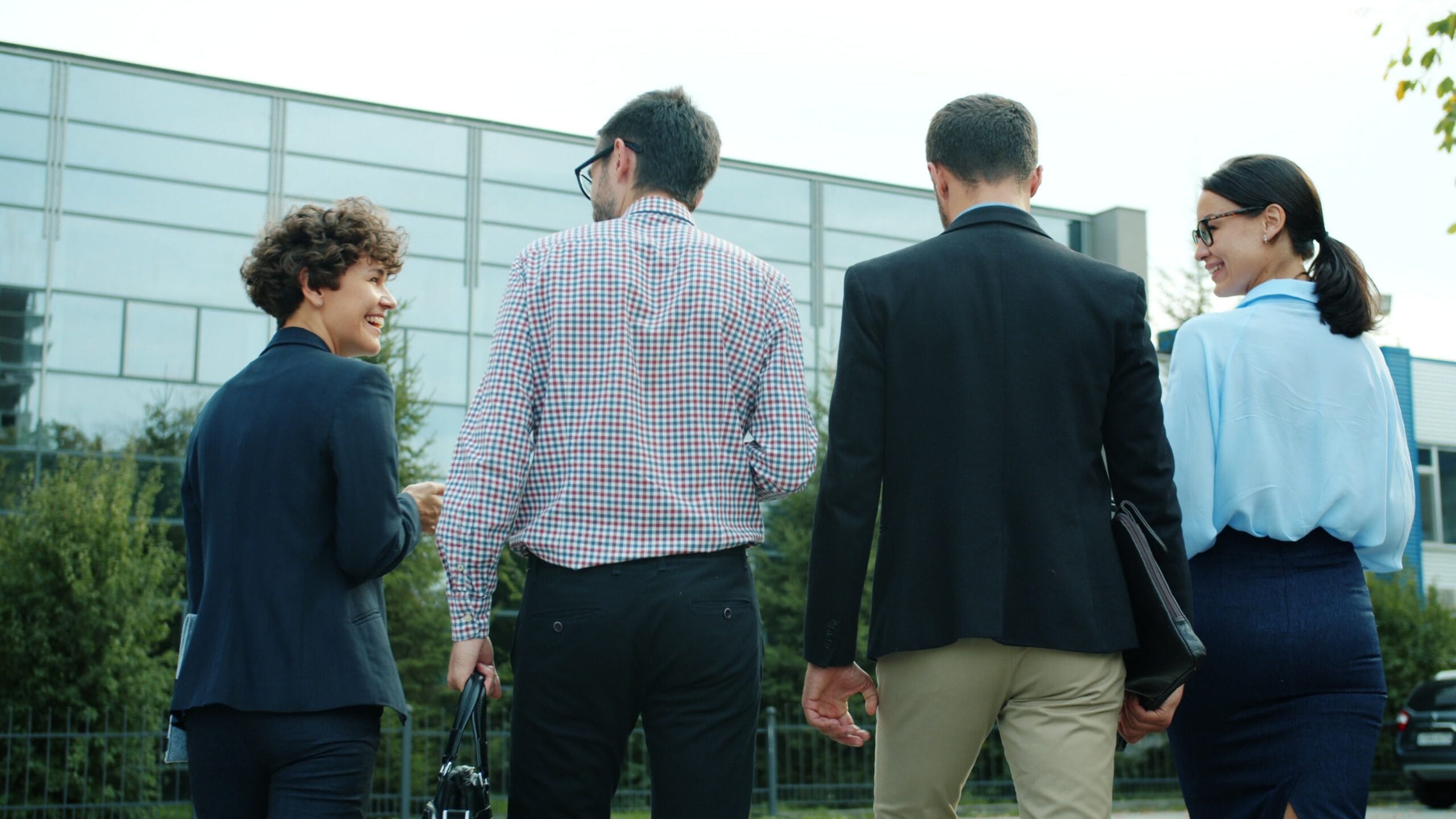 Quatre professionnels en tenue d'affaires discutent dehors devant un bâtiment moderne vitré, illustrant une initiative de team building RSE en environnement de travail.