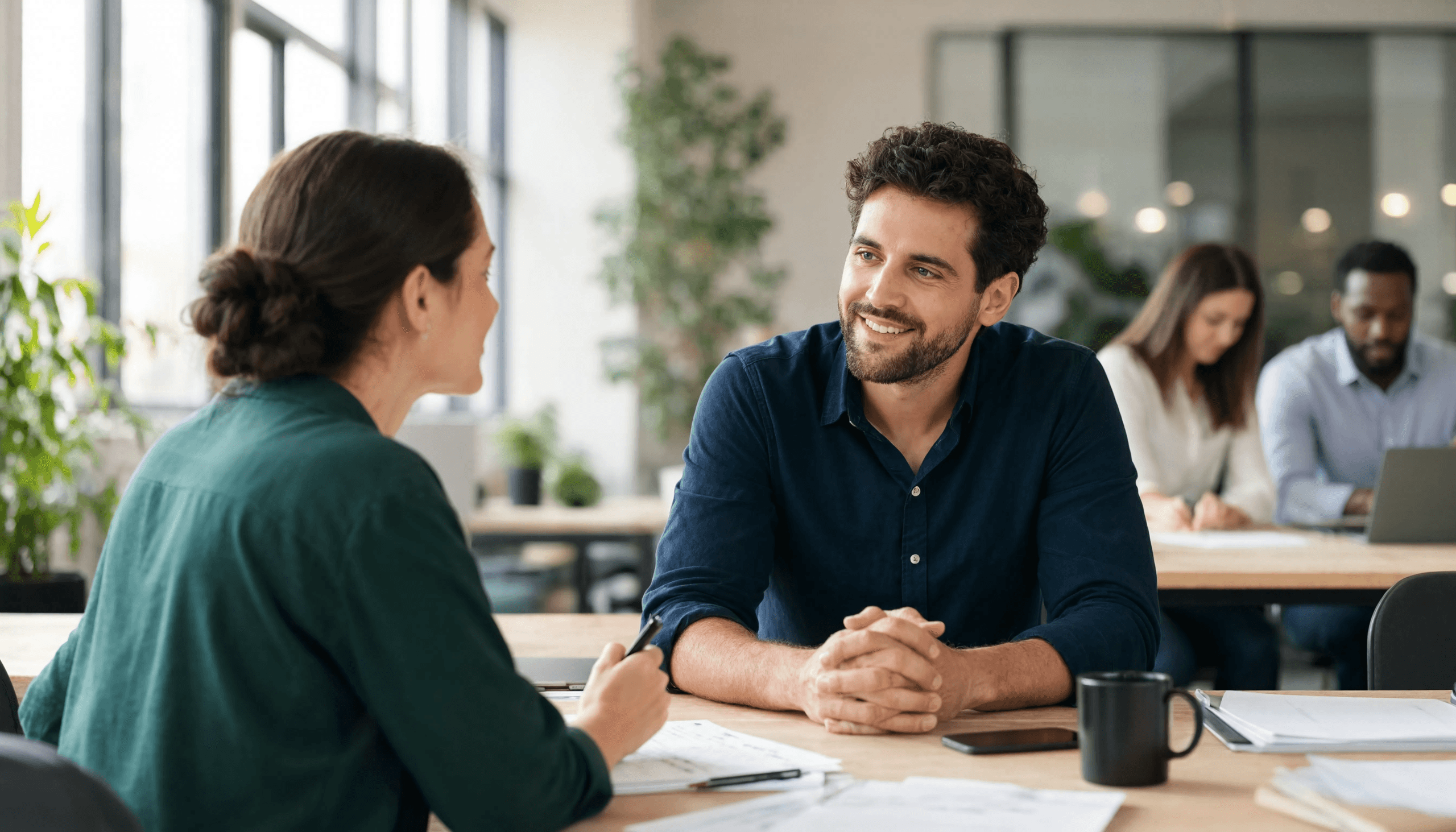 Deux professionnels en discussion dans un open-space lumineux, illustrant le bien-être et la communication positive entre managers et équipe au travail.