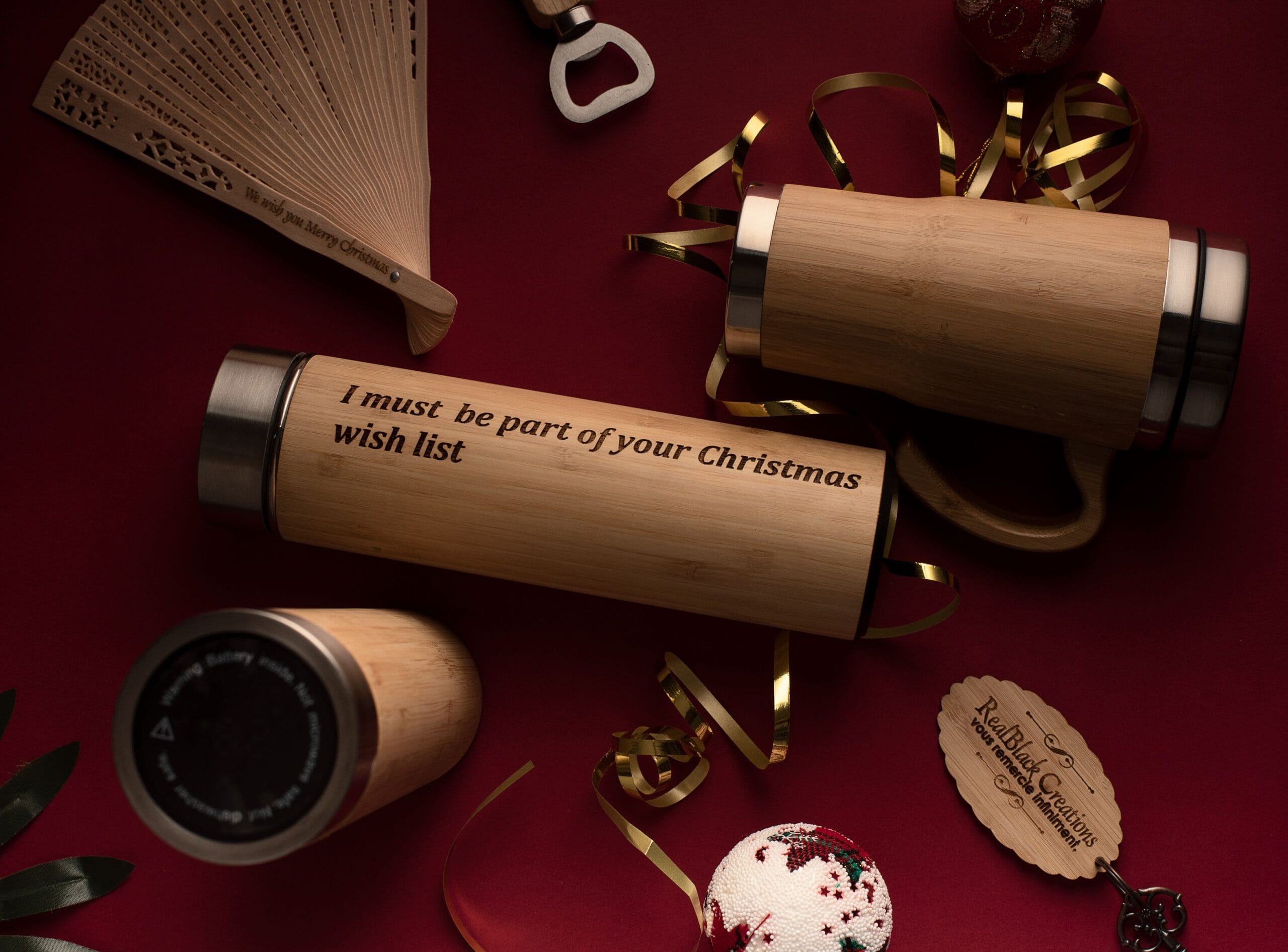 Parchemins en bambou gravés avec message de vœux de Noël, entourés de rubans dorés, d'un ventail ajouré, d'une boule de Noël et d'accessoires festifs sur fond bordeaux.