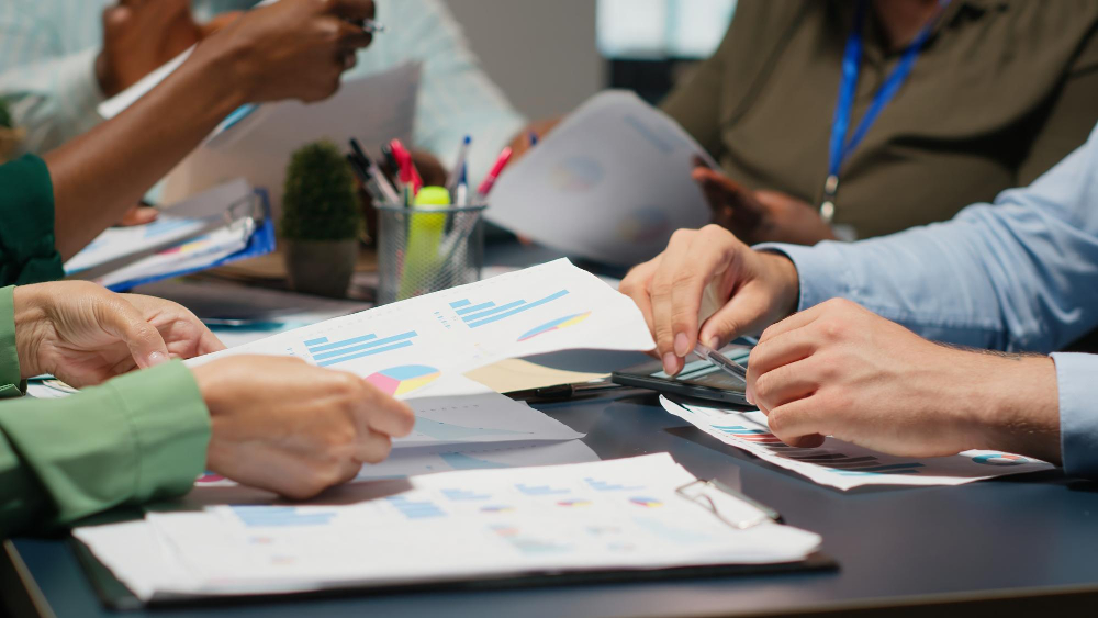 Équipe analysant ensemble des graphiques et données financières colorées autour d'une table de réunion, avec stylos et documents de travail.